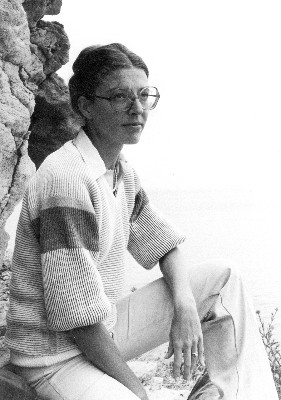 Das Schwarz-Weiß-Foto zeigt Frau Marita Kersken-Bradley sitzend auf einem Steinvorsprung. Sie hat ihre Haare zu einem Dutt gebunden, trägt eine Brille und schaut, mit dem linken Arm auf das Bein abgelegt, in die Ferne.