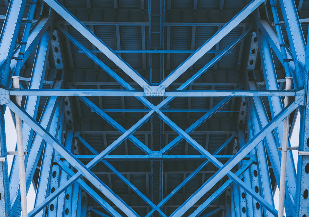 Die Aufnahme zeigt eine eine hellblaue Metallbrücke mit Fachwerk und darüberliegender Fahrbahn.