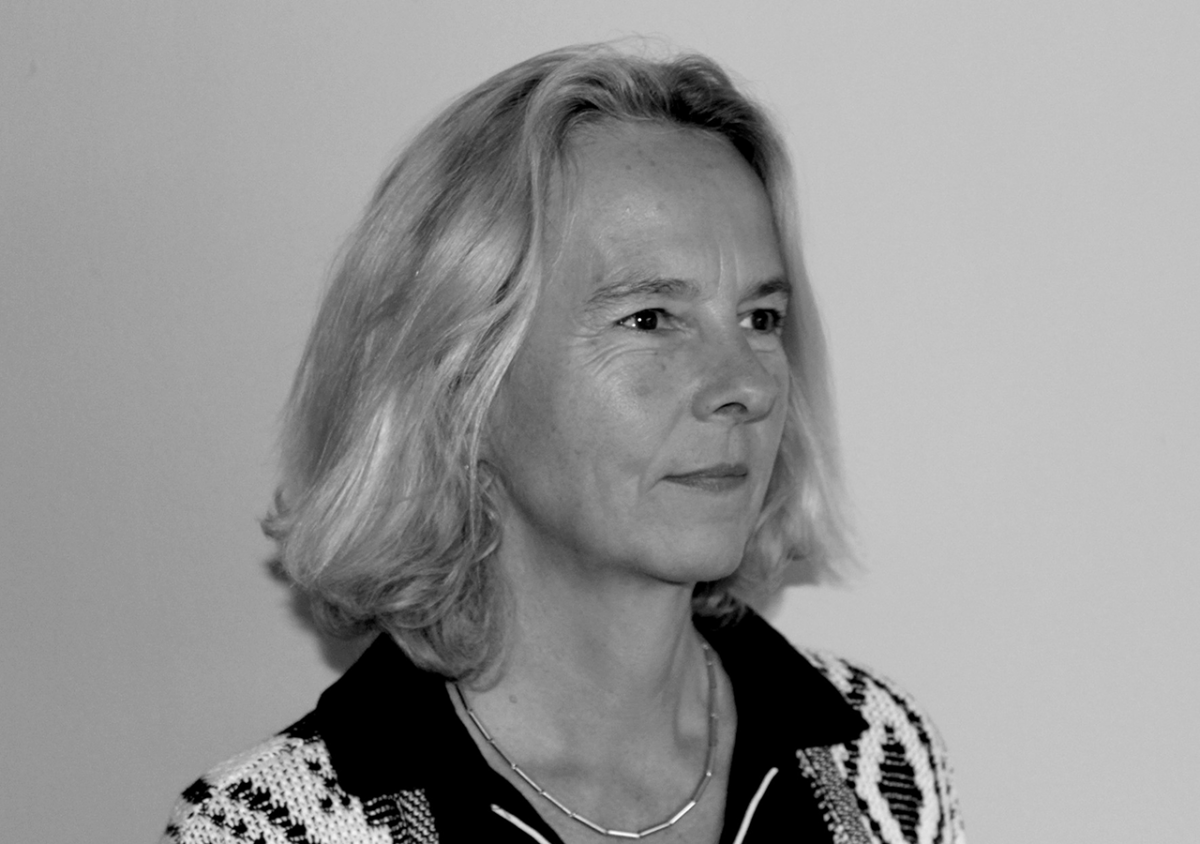 Auf dem schwarz-weiß Porträt ist Frau Martina Schnellenbach-Held aus der Dreiviertel-Perspektive, vor einem hellen Hintergrund zu sehen. Sie hat blonde, schulterlange Haare und trägt eine Kette um den Hals.
