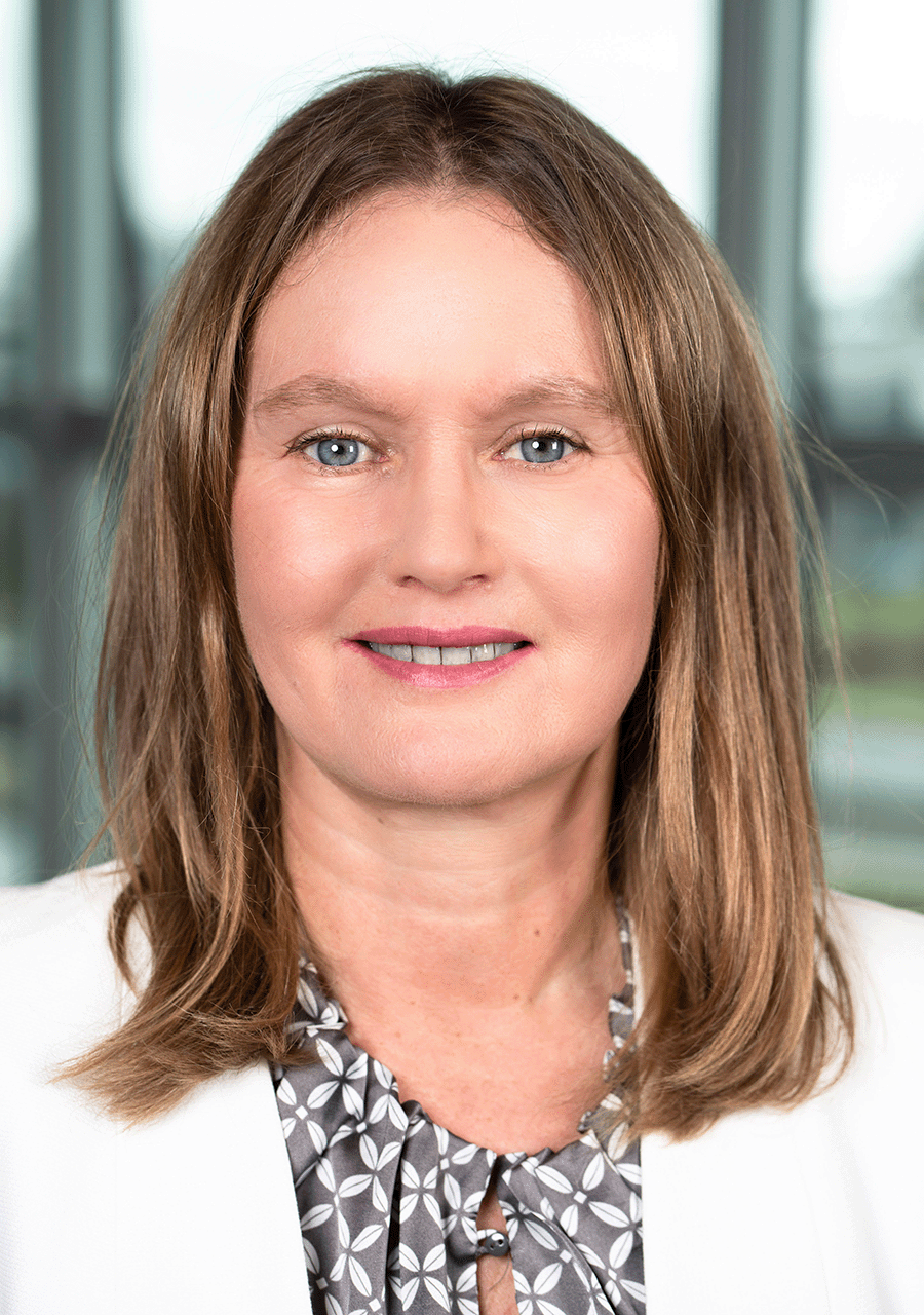 Das dargestellten Portät zeigt Dr. Katja Hüske mit leicht nach rechts gedrehtem Kopf, dabei blickt sie direkt in die Kamera. Sie trägt ihre hellen Haare schulterlang, dazu einen weißen Blazer über einer grau-weiße Bluse.