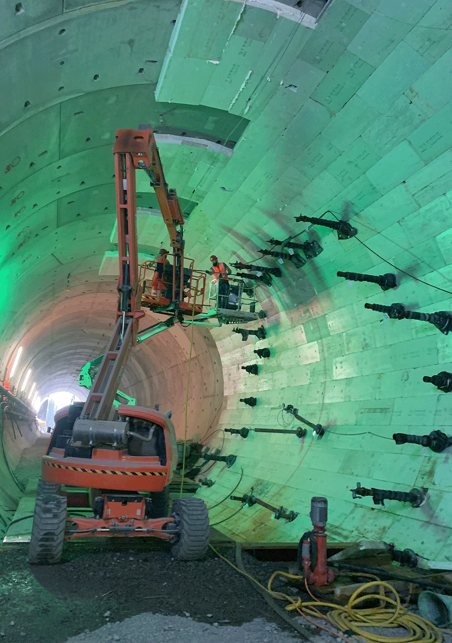 Zu erkennen ist eine Tunnelbaustelle in Rastatt. Darin sind eine Hubbühne sowie Bauarbeiter im Einsatz, die gerade die Vereisungsleitungen des Tunnels bearbeiten. 